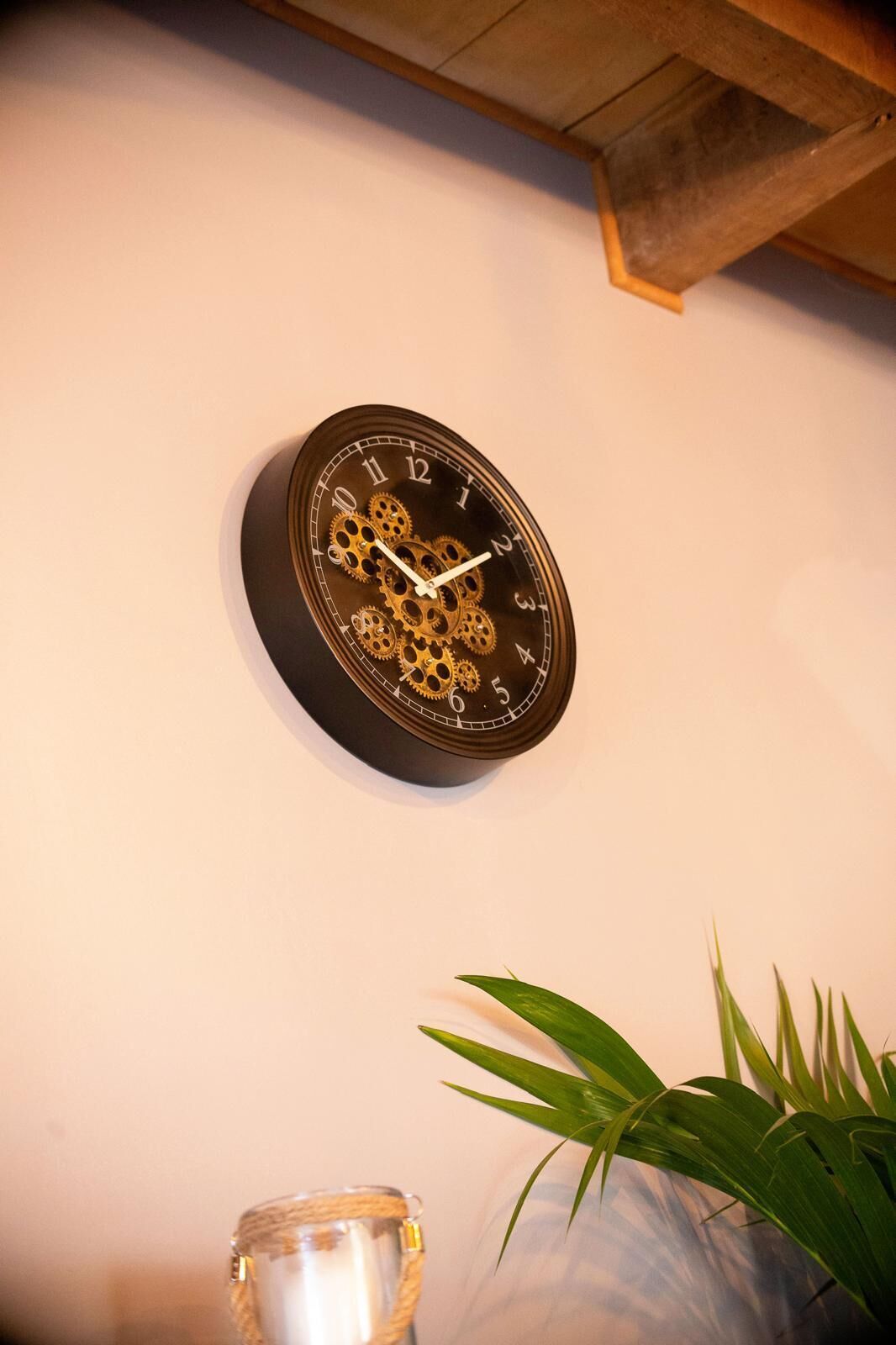 A wall-mounted clock with a mechanical design, a candle holder, and a potted plant.