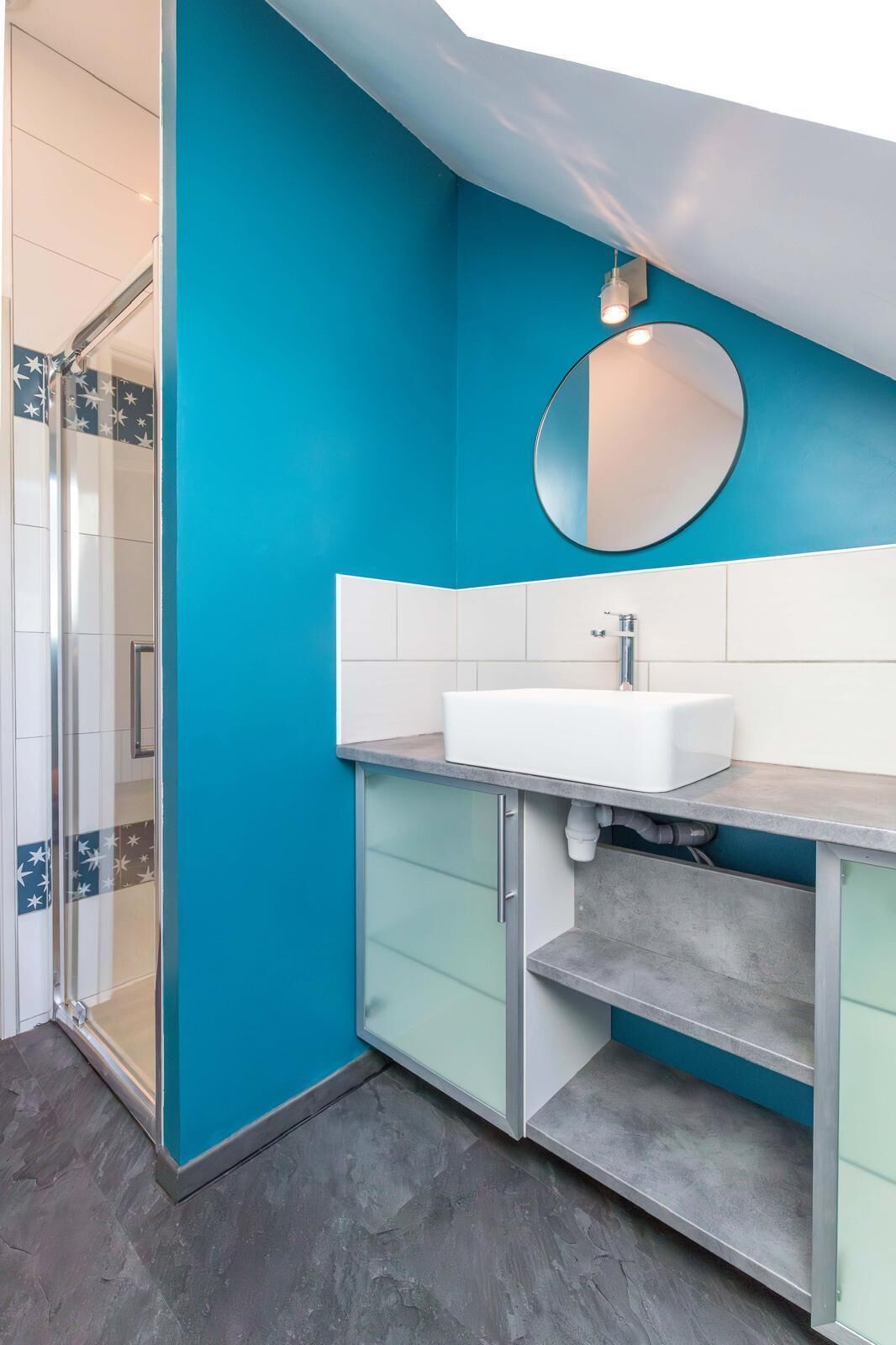 Een badkamer met een blauwe wand, een witte wastafel en een glazen douchecabine.