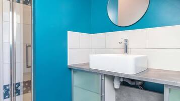 Een badkamer met een blauwe wand, een witte wastafel en een glazen douchecabine.