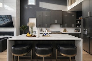 Une cuisine moderne avec des meubles de couleur sombre, un îlot en marbre et trois tabourets de bar noirs.