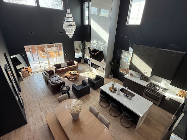 Un espace de vie et de salle à manger moderne, ouvert et décloisonné, comprenant une grande table à manger, des canapés et une cuisine dotée de meubles de couleur sombre.