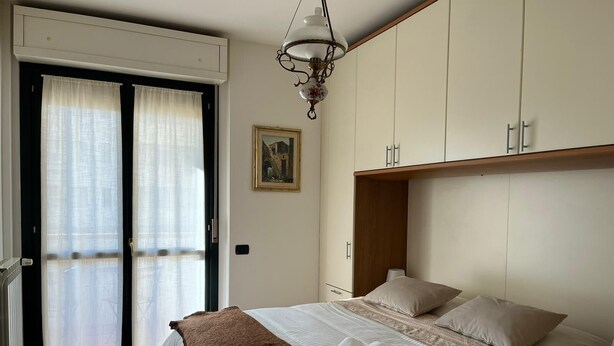 A bedroom with a bed, a wooden wardrobe, a ceiling light fixture, and a door with curtains.