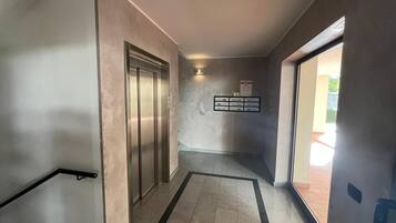 Un couloir avec un ascenseur, un panneau de déclenchement d’alarme incendie et une porte donnant sur l’extérieur.