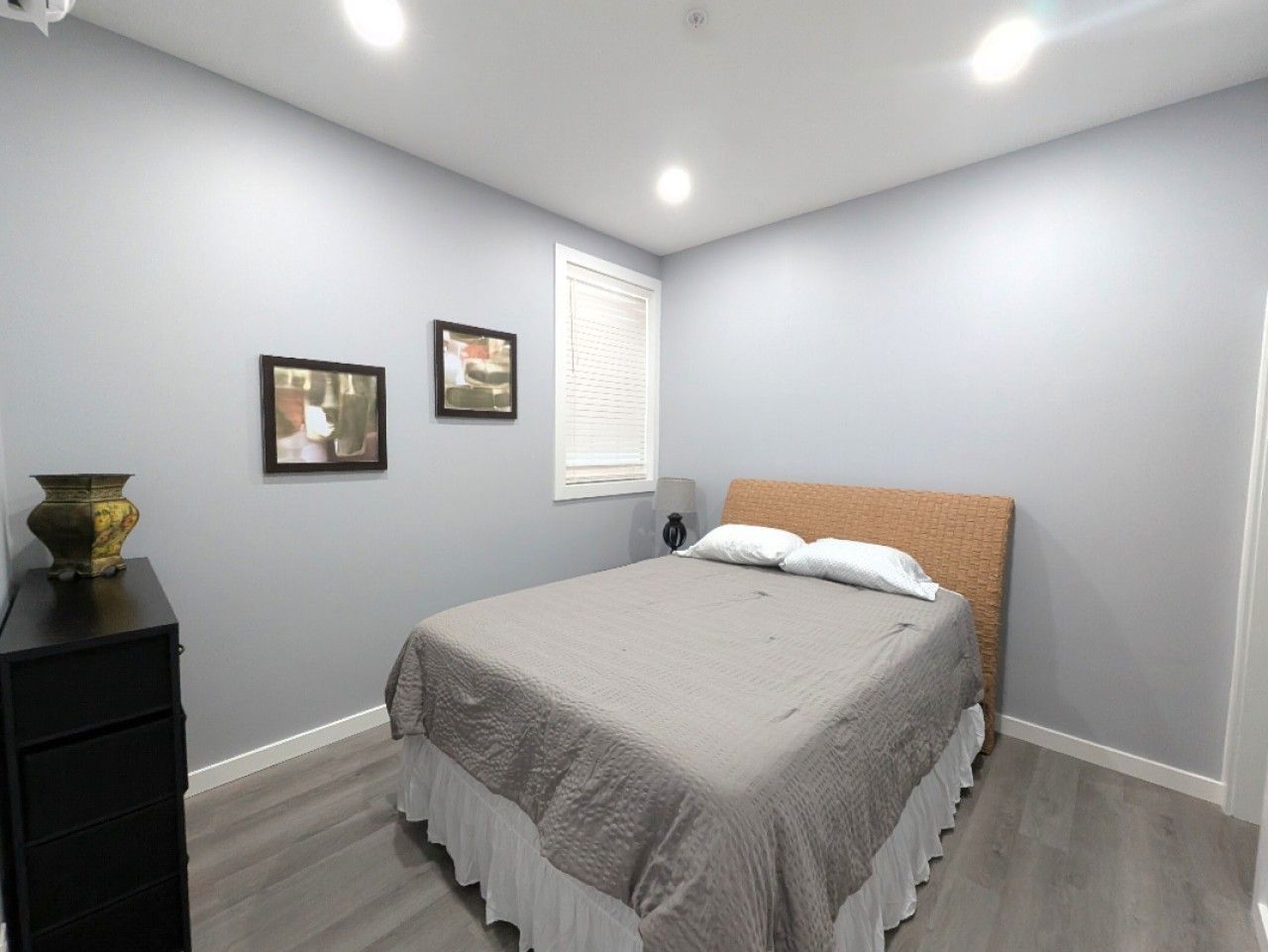 Een slaapkamer met een bed, een dressoir en twee ingelijste foto’s aan de muur.