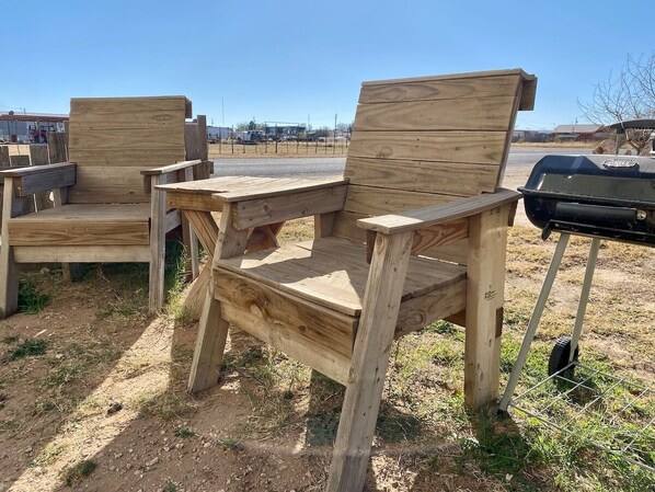 A wooden bench with a backrest and armrests, placed outdoors on a dirt ground.