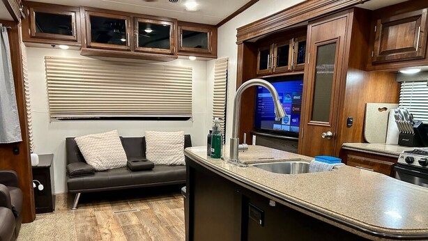 A compact RV kitchen with a built-in sink, a stove, and a small dining area with a couch.