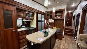A compact kitchen with wooden cabinets, a microwave, a sink, and a stove.