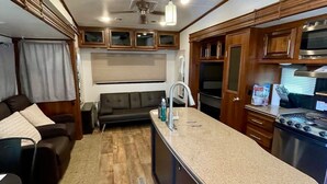 A compact RV kitchen with a central island, wooden cabinets, a built-in stove, and a seating area with a sofa and chairs.