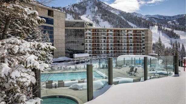 Um hotel com área de piscina, rodeado por árvores e montanhas cobertas de neve.