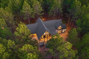 Une grande cabane à deux étages, entourée d’une forêt dense.