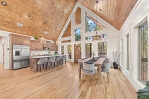 A spacious kitchen with a large island, wooden ceiling, and large windows.