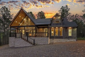 A large, modern house with a prominent front porch, multiple large windows, and a stone foundation.