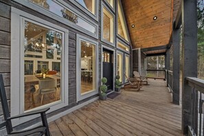 A wooden deck with outdoor seating, large windows, and a covered area.