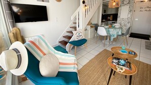 A modern living room with a sofa, a television, and a staircase leading to a dining area.