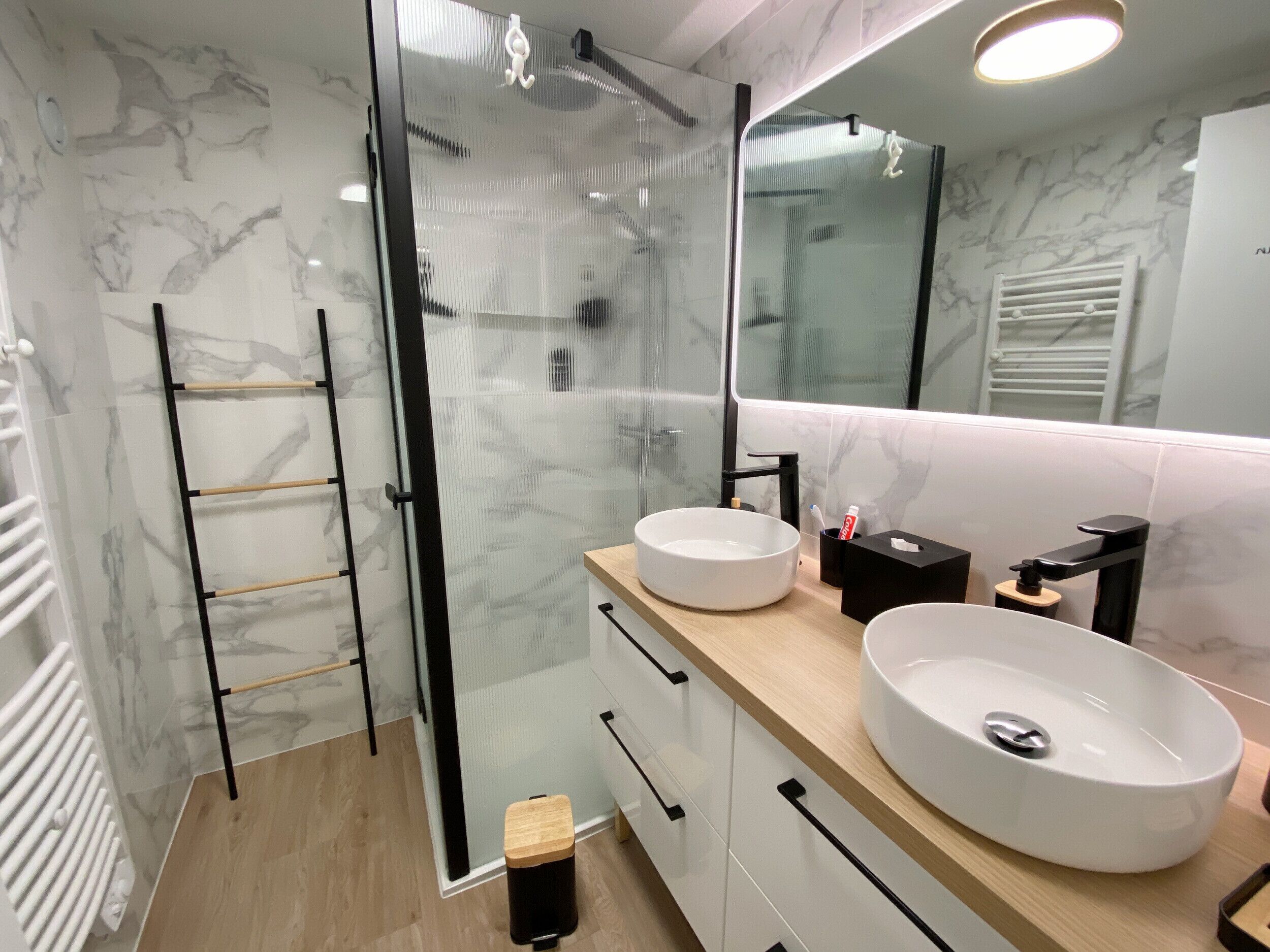 Een moderne badkamer met een douchecabine van glas, twee wastafels en een grote spiegel.