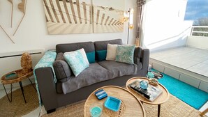 A modern living room with a grey sofa, blue and white patterned cushions, a wooden coffee table with a blue candle, and a woven side table.