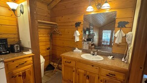 Baño de cabaña de madera con lavamanos, espejo y perchero para toallas.