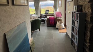 A spacious hallway with a high ceiling, wooden beams, and a stone wall. There is a cozy seating area with a couch and chairs, a bookshelf, and a view of the outdoors. - Stunning views beautiful old farmhouse Peaceful overlooking  bay & mountains (Tuosist)