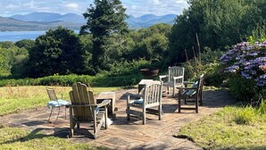 An outdoor patio with stone flooring and wooden furniture, overlooking a scenic landscape with mountains and a body of water. - Stunning views beautiful old farmhouse Peaceful overlooking  bay & mountains (Tuosist)