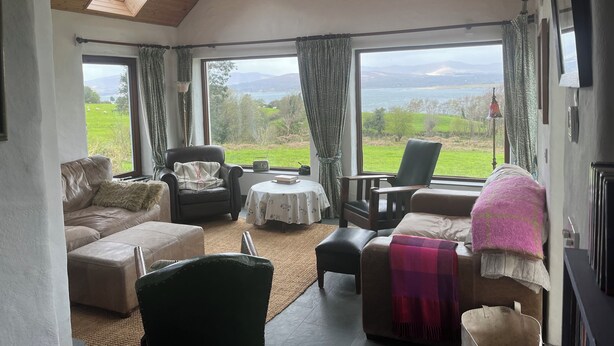 A cozy living room with a wooden ceiling, large windows offering a scenic view, a sofa, chairs, and a table. - Stunning views beautiful old farmhouse Peaceful overlooking  bay & mountains (Tuosist)