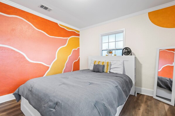 A bedroom with a bed, a window, and a wall with abstract orange and white patterns. - Charming 3-bedroom cottage with WiFi and AC in Foley (Foley)