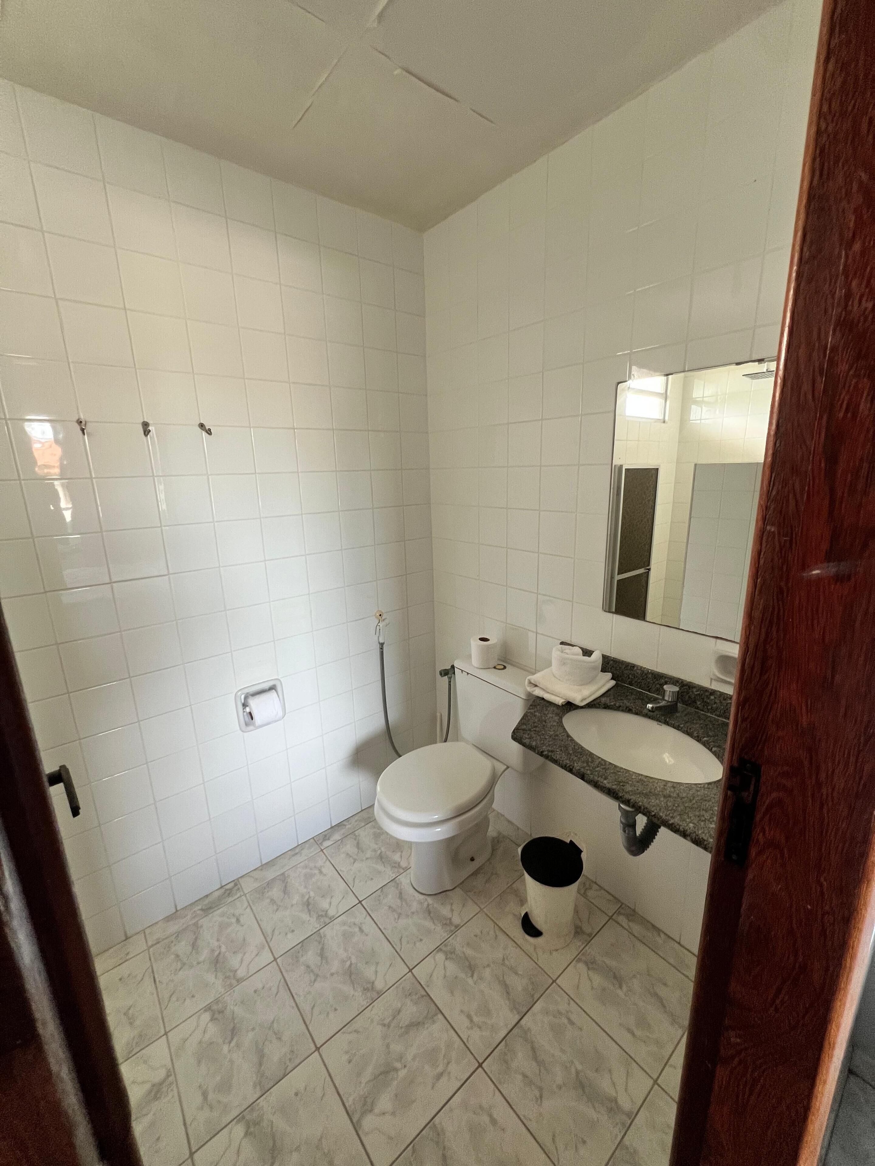 Ein Badezimmer mit weißen Fliesen, einer weißen Toilette, einem Waschbecken mit Spiegel und einer Duschkabine.