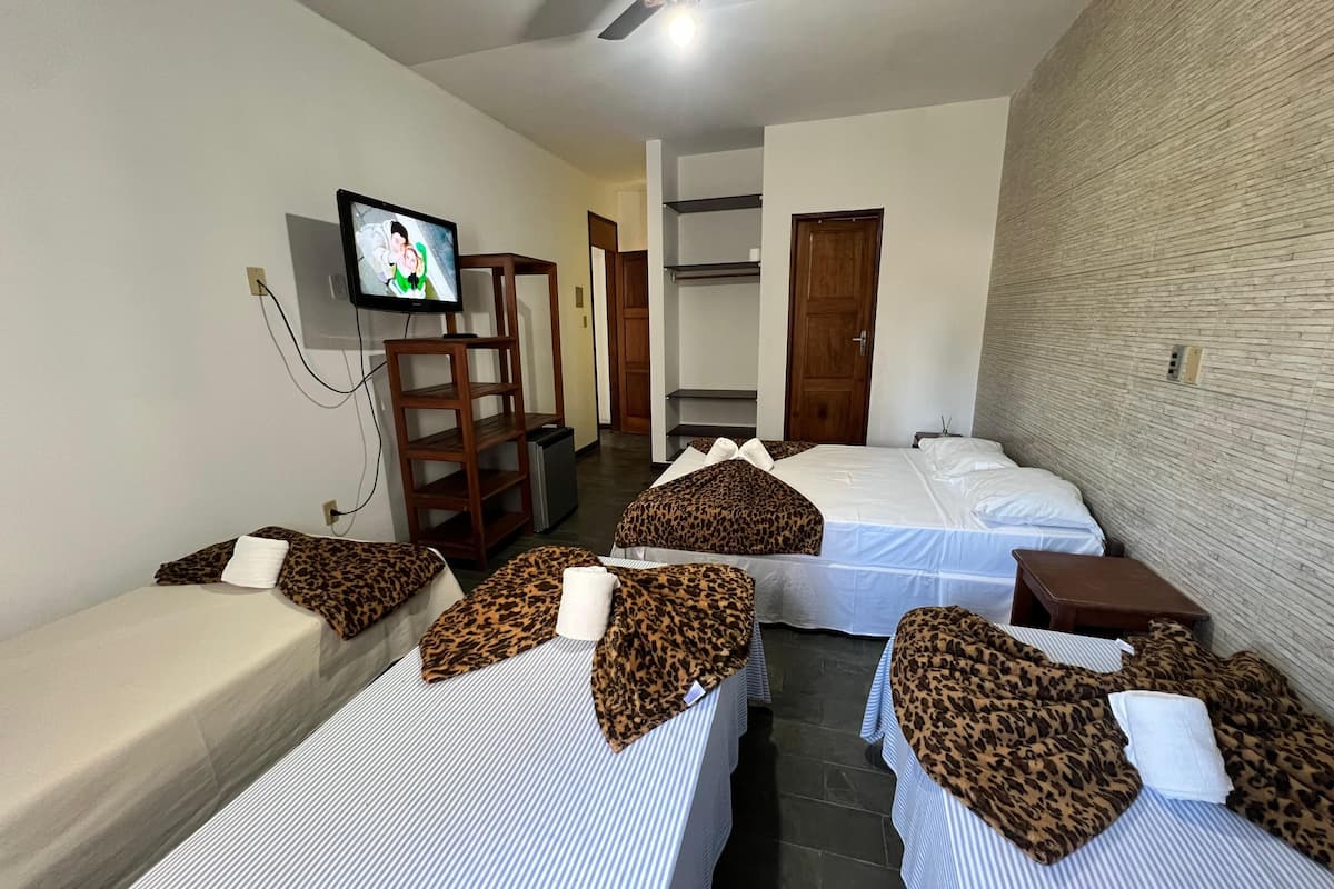 A hotel room with two beds, a television, a ceiling fan, and a brick wall.