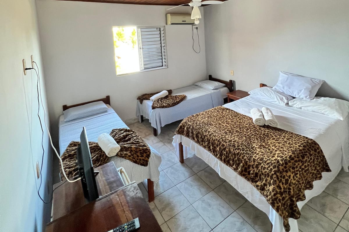 A hotel room with two single beds, a double bed, a TV, and a ceiling fan.