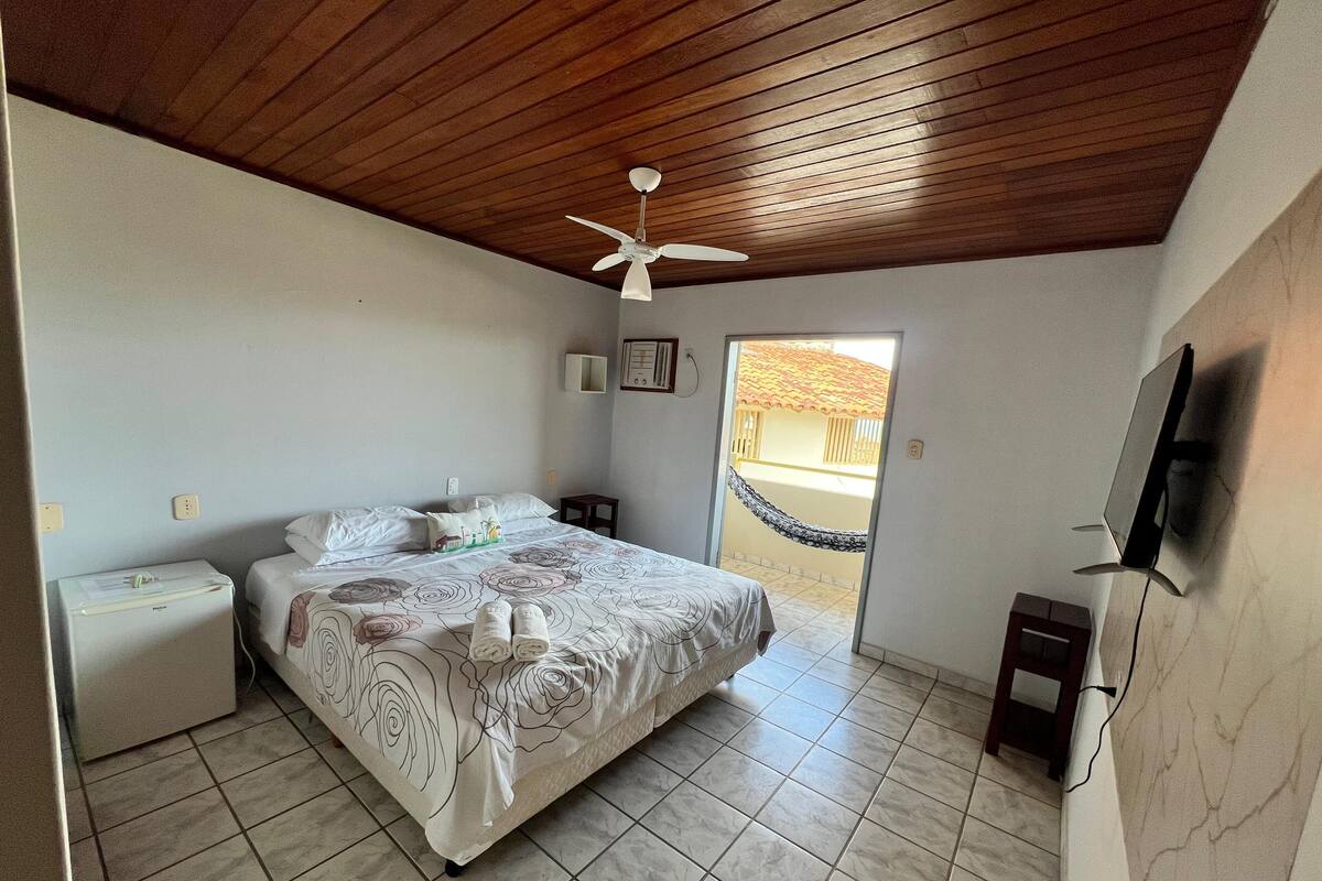 A bedroom with a bed, a nightstand, a ceiling fan, a TV, and a view of the outside.