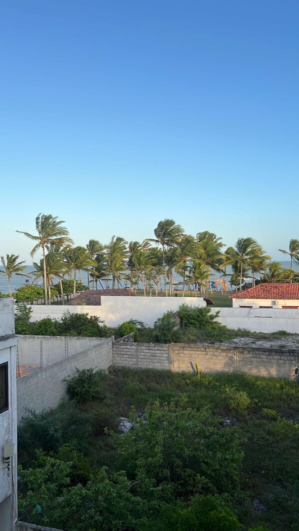 A coastal view with palm trees, a beach, and a building with a red roof. - Pousada Orla Do Sol (Prado)