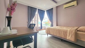 A hotel room with a bed, a desk, a chair, a vase with flowers, and a window with curtains.