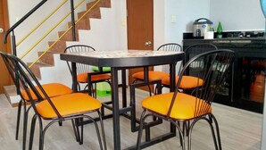A dining area with a round table and six chairs, a staircase, and a kitchen area with a kettle and a bottle.