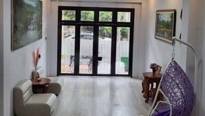 Un amplio salón con un gran ventanal corredera que da a un espacio exterior, un sillón colgante y un sofá.