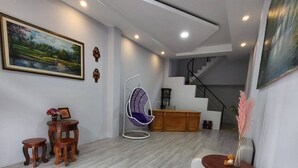 Una sala moderna con un sofá blanco, un sillón colgante y una mesita con un florero. Se ve una escalera al fondo.
