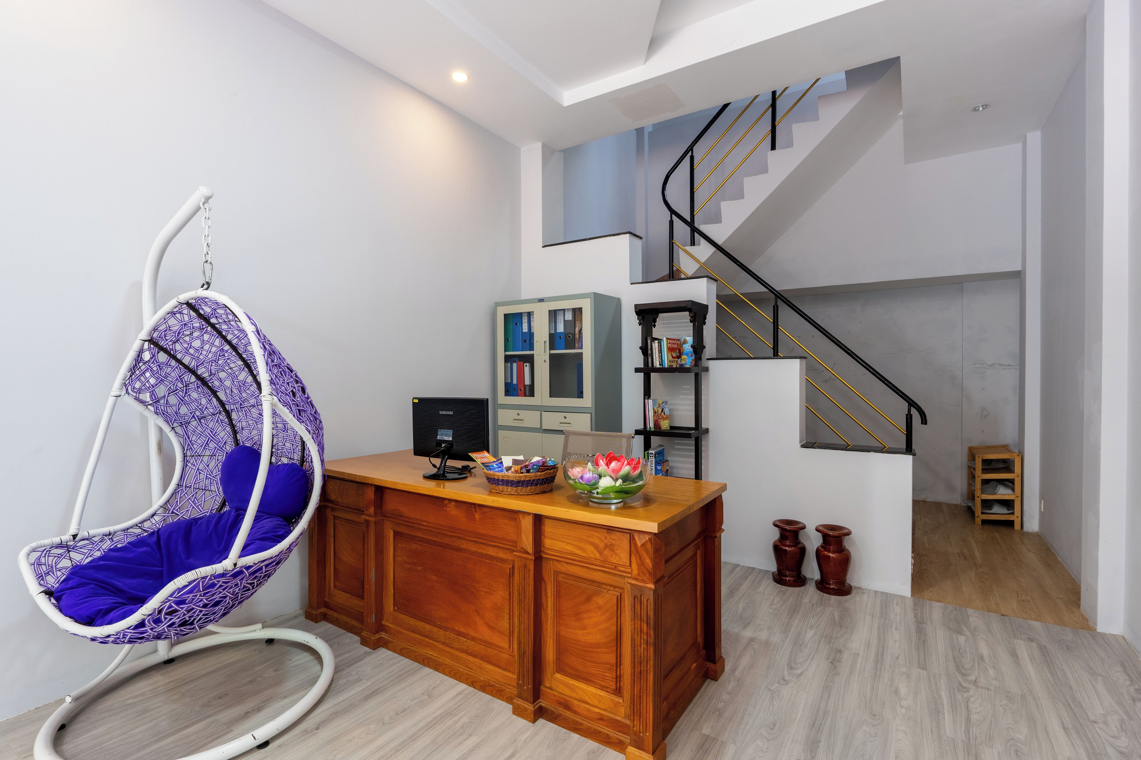 Een modern interieur met een hangstoel, een houten bureau, een computer en een trap.