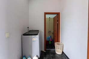 A compact bathroom with a washing machine, a shower, and a laundry basket. - Bright 2BR House • Central Phnom Penh • Sleeps 4 • Workspace • Laundry (Phnom Penh)