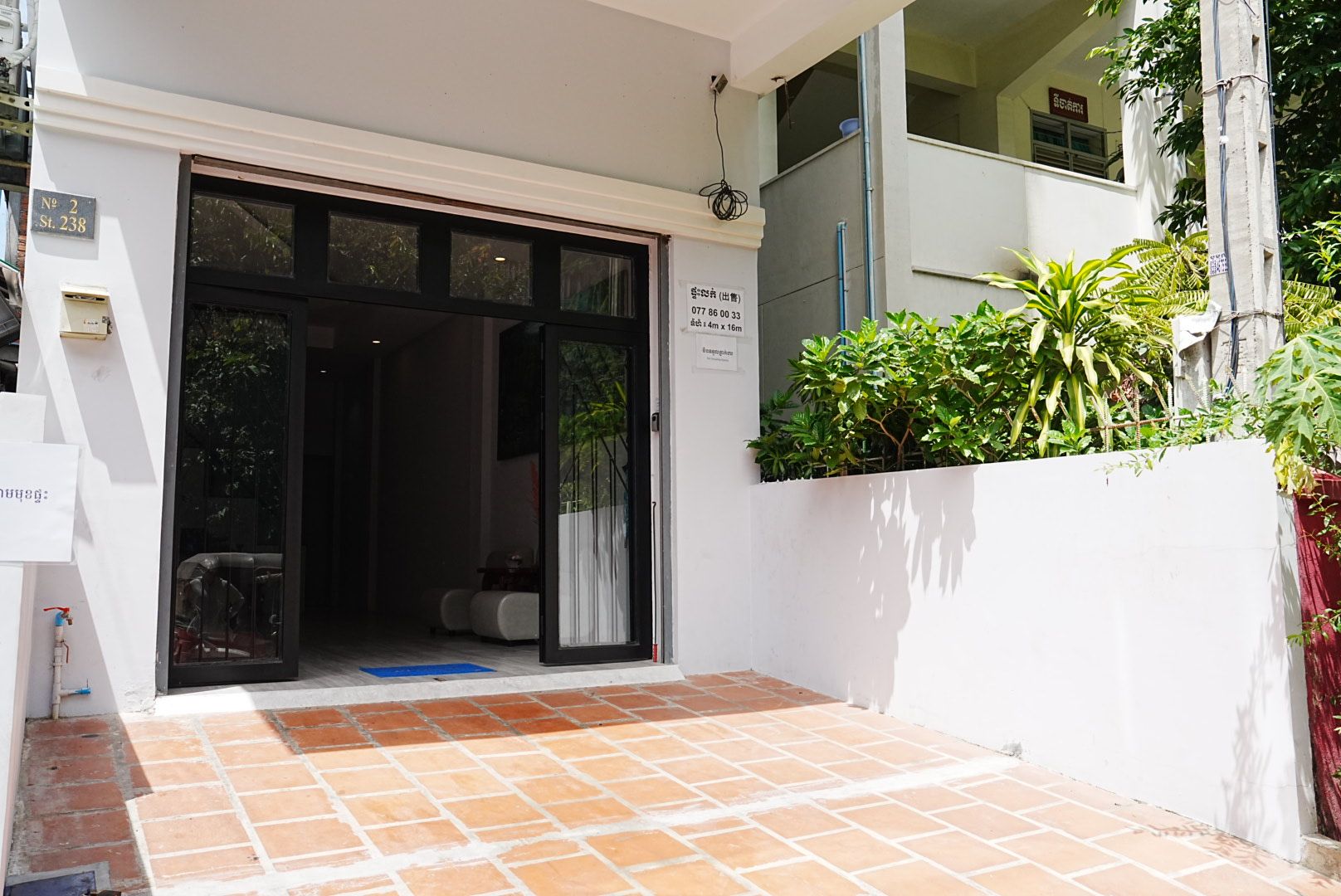 A building entrance with a tiled patio, a glass door, and a white wall with a sign.