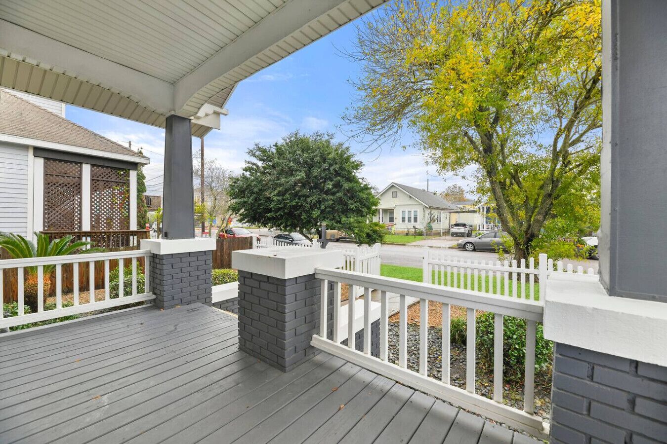 Eine überdachte Veranda mit Holzdeck, weißen Geländern und einer Backsteinmauer.