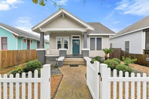 A residential house with a front porch, a small garden, and a white picket fence.