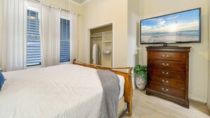 Ein Schlafzimmer mit einem Bett, einem Schminktisch, einem Fernseher und einem Fenster mit Vorhängen.