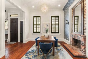 A dining room with a wooden table, blue chairs, a patterned rug, and a brick fireplace.