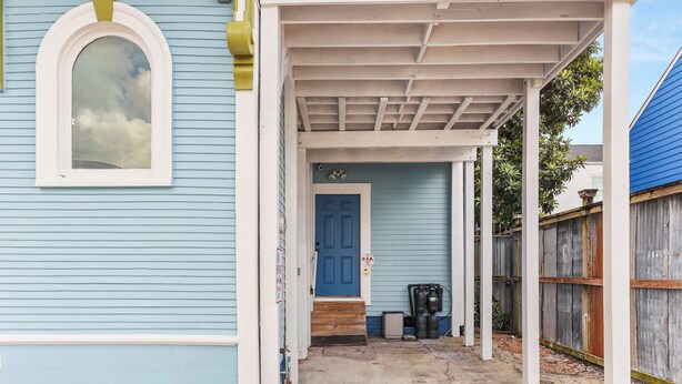 Un porche abrité, doté d’une porte bleue et d’un escalier menant à une maison dont le revêtement extérieur est d’un bleu clair.