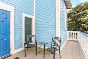 A blue house with a white door, a small porch with two chairs and a table, and a white railing.