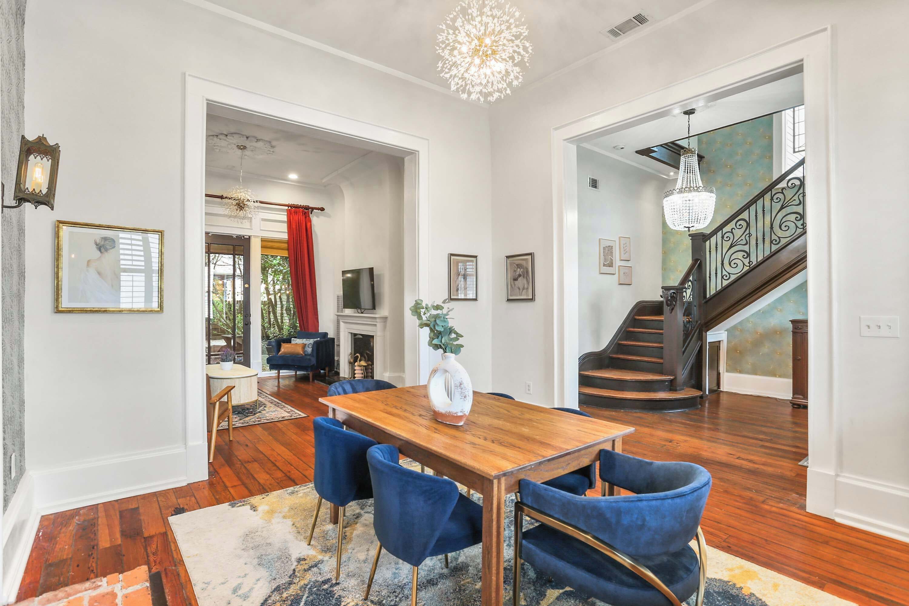 A dining area with a wooden table and blue chairs, a chandelier, and a staircase leading to another level.