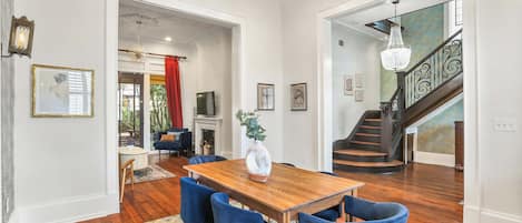 Un espace repas avec une table en bois et des chaises bleues, un lustre et un escalier menant à un autre niveau.