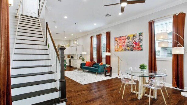 A spacious living area with a staircase, a dining table with chairs, a sofa, and a kitchen in the background. - Designer's Dream! 3 bed/2.5 bath (New Orleans)