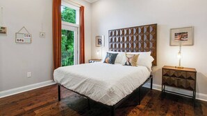 A bedroom with a bed, a nightstand, a window with curtains, and wall-mounted pictures. - Designer's Dream! 3 bed/2.5 bath (New Orleans)