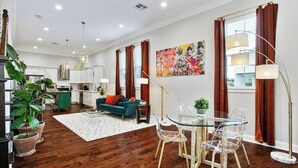A modern living room with a glass dining table, a sofa, and a kitchen in the background. - Designer's Dream! 3 bed/2.5 bath (New Orleans)