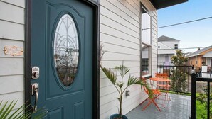 A teal front door with a glass panel, a potted plant, and outdoor furniture on a wooden deck. - Designer's Dream! 3 bed/2.5 bath (New Orleans)