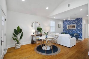 Un salon spacieux avec une table ronde, un canapé blanc et un mur orné d’un motif bleu.